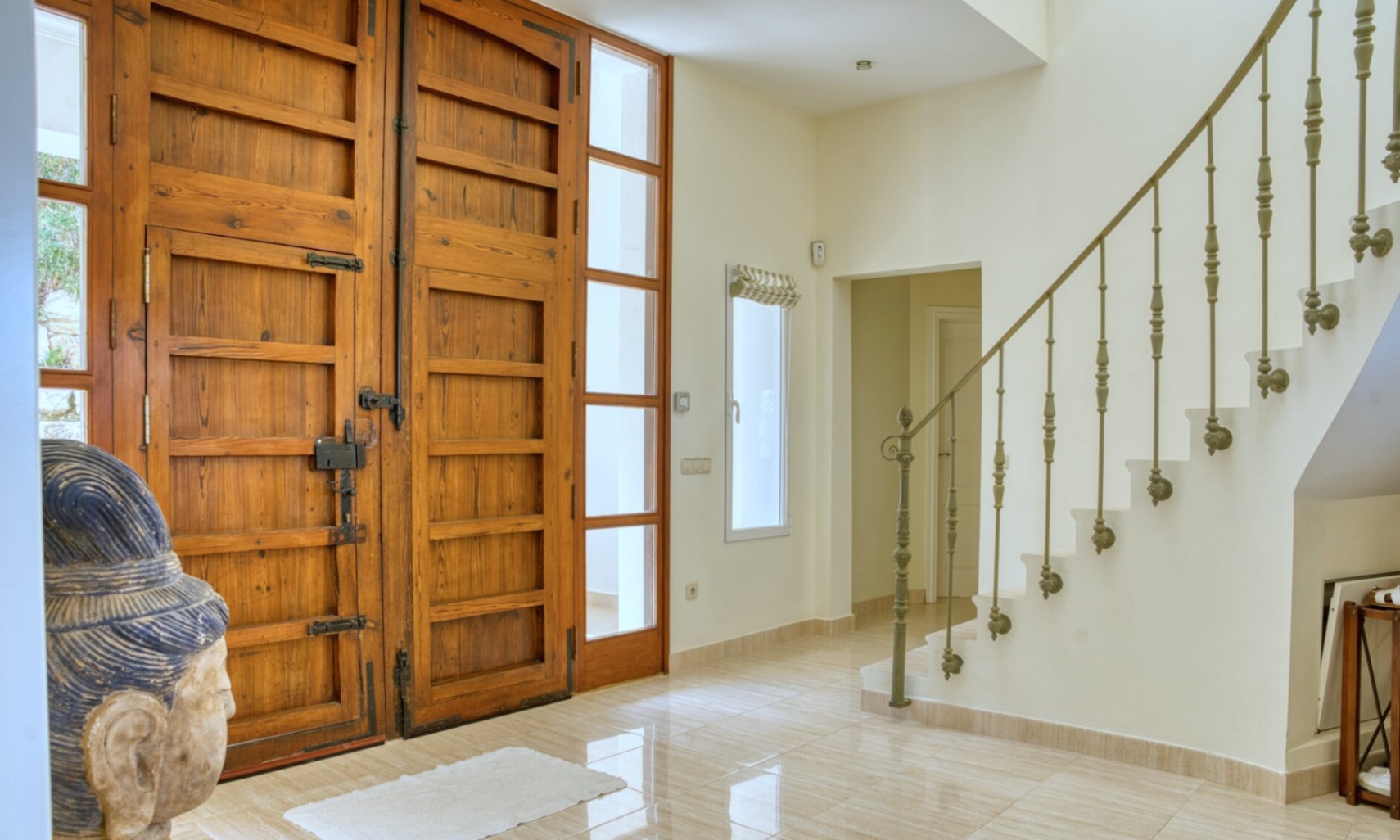 Entrance hall featuring rustic wooden double doors with wrought iron hardware, polished tile flooring, and a staircase with a decorative metal railing.