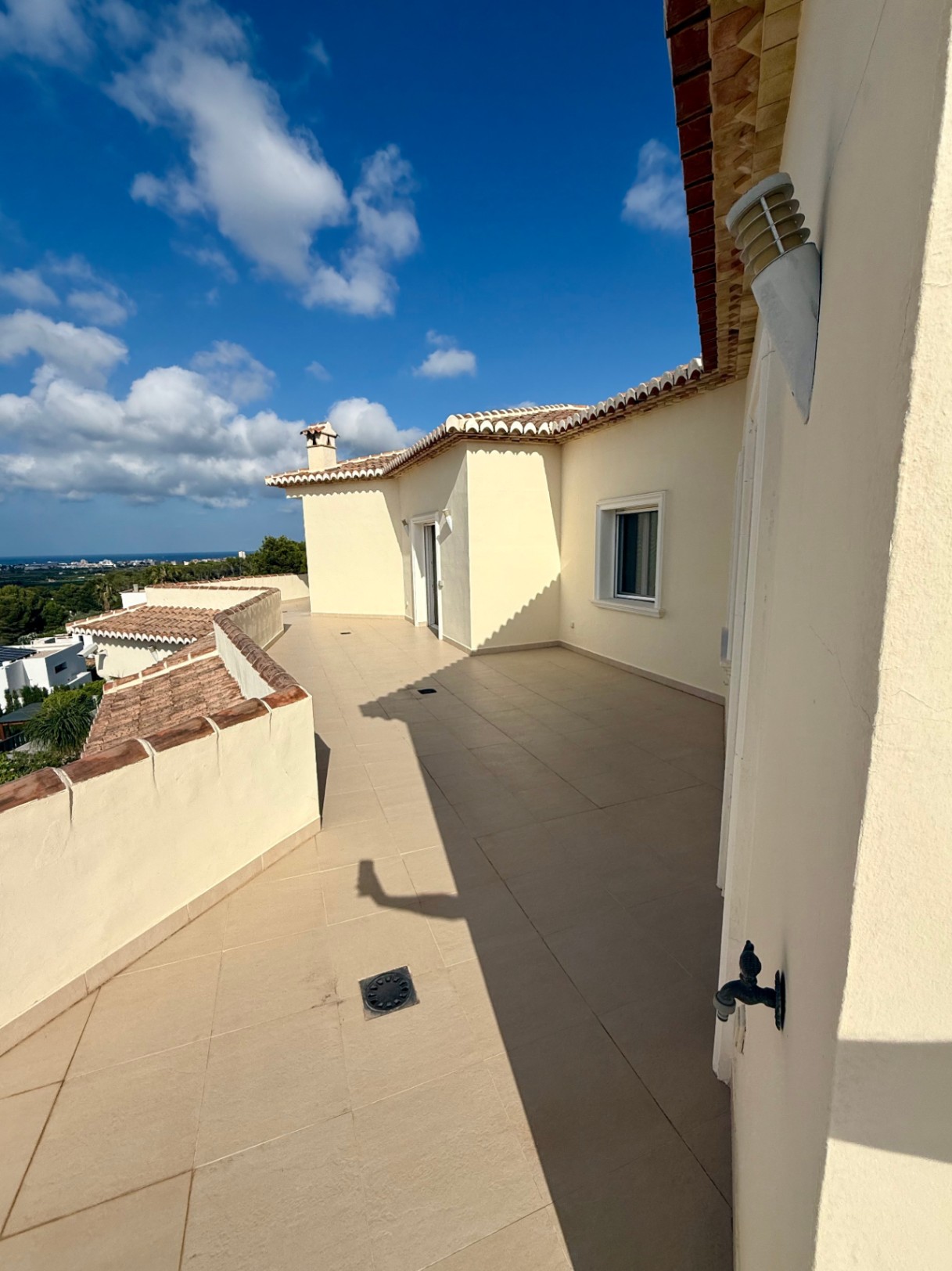 Expansive upper-level terrace featuring beige tiling and panoramic Mediterranean views. The curved layout follows the villa's architecture with traditional roof tiles.