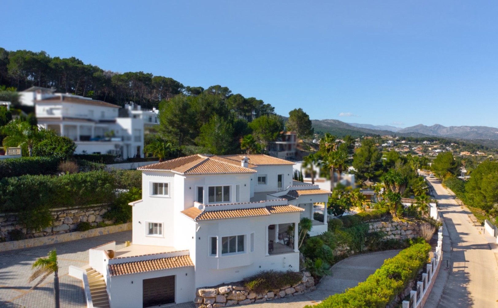 Exterior view of the Mediterranean-style villa featuring white facades, terracotta roof tiles, and an integrated garage, set against stone retaining walls in Piver.