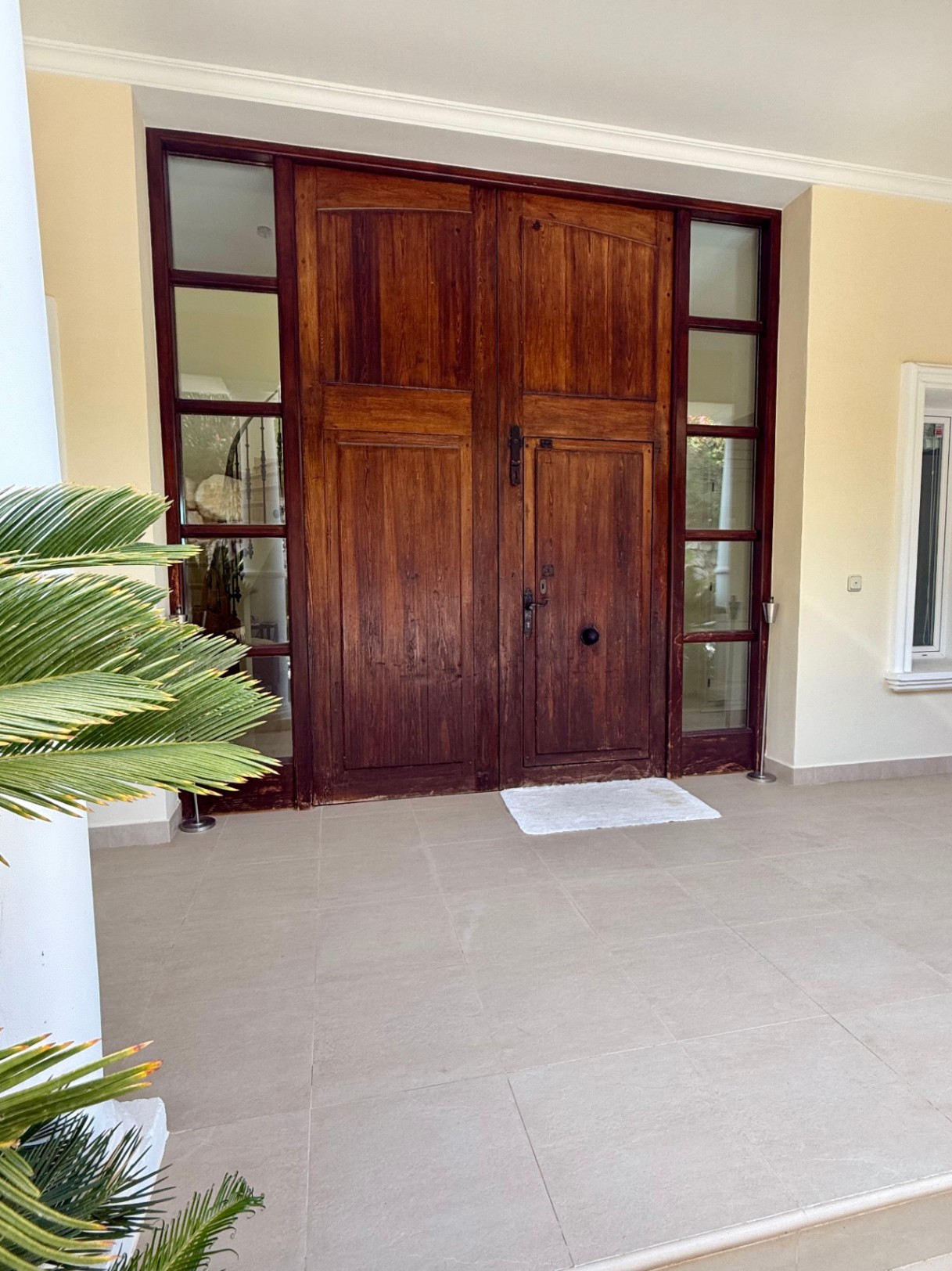 Grand entrance featuring a massive solid wood double door with integrated access, flanked by vertical glass sidelights on a neutral tiled porch.