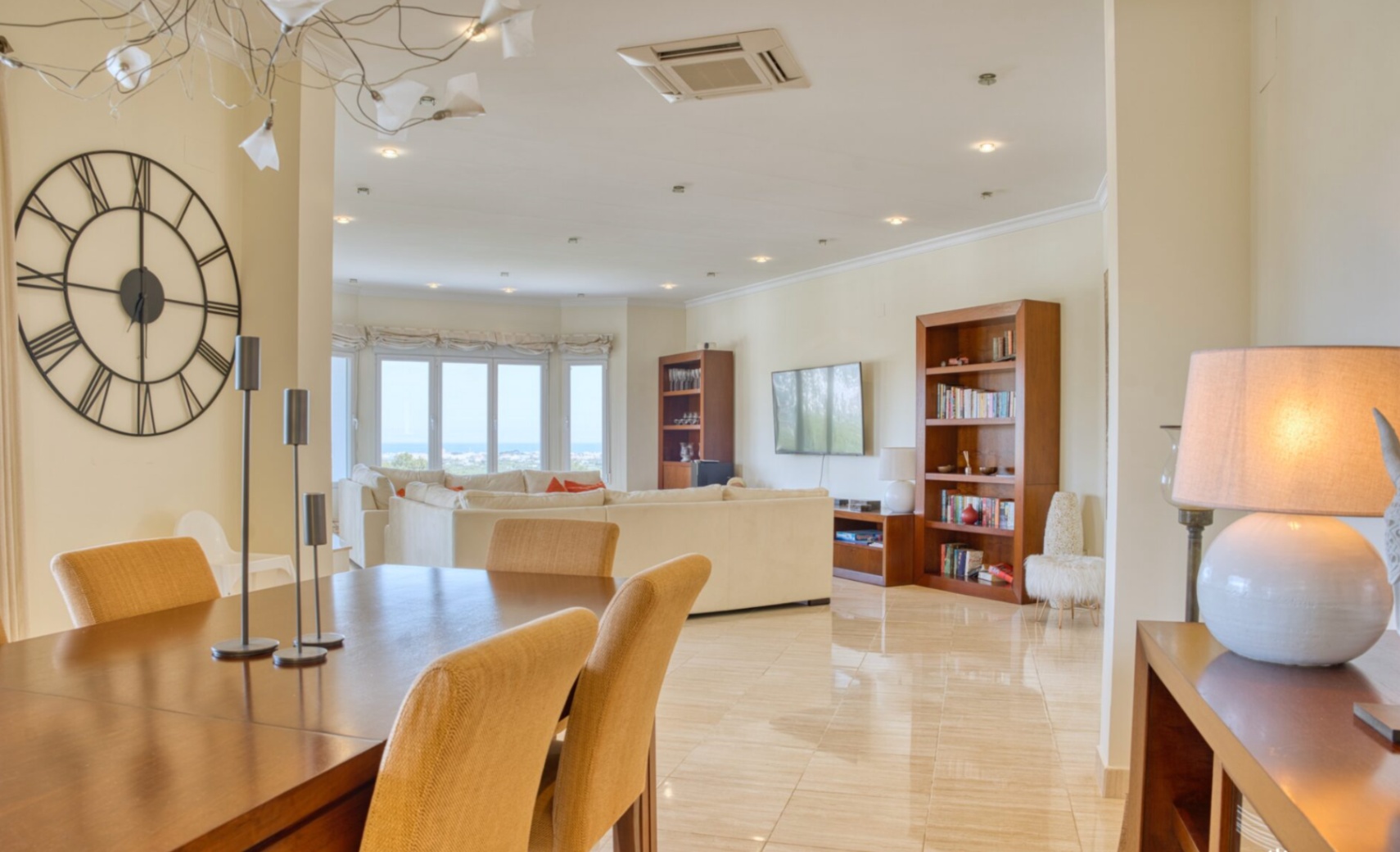 Open-plan living and dining area featuring polished marble floors, wooden cabinetry, and large windows overlooking the Mediterranean coast.