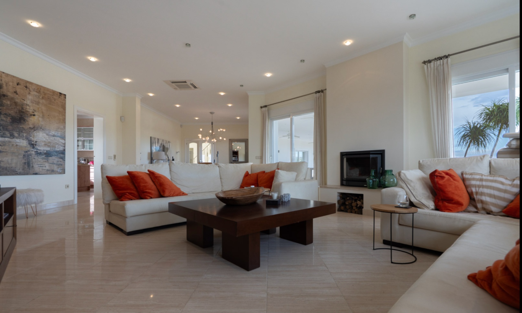 Spacious living room featuring polished marble floors, a built-in fireplace, and large sliding doors. The open layout includes white sectional seating and recessed ceiling lighting.