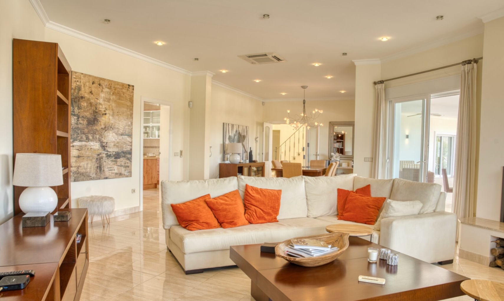 Spacious living room featuring polished marble floors, a large white sectional sofa with orange accents, and floor-to-ceiling glass doors opening to the terrace.