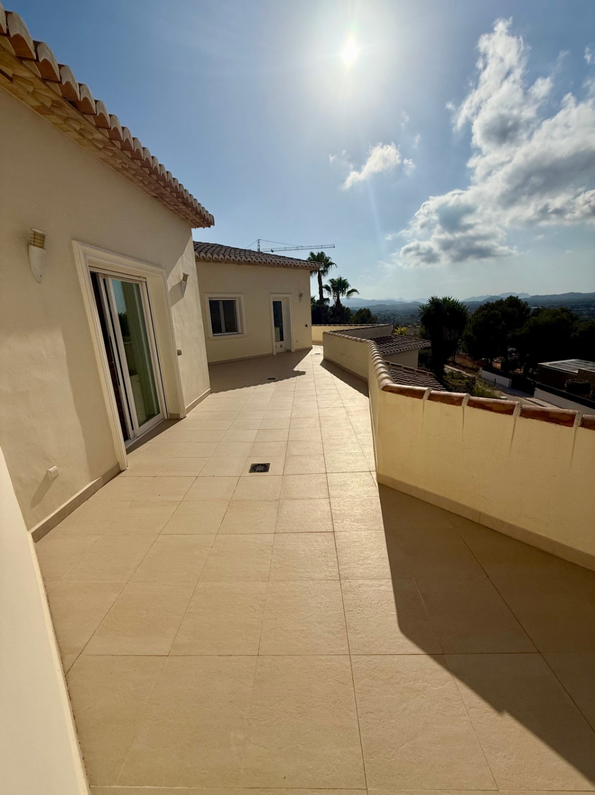 Spacious upper terrace featuring beige ceramic tiling and a low perimeter wall, offering panoramic views of the valley and distant mountains under bright sunlight.